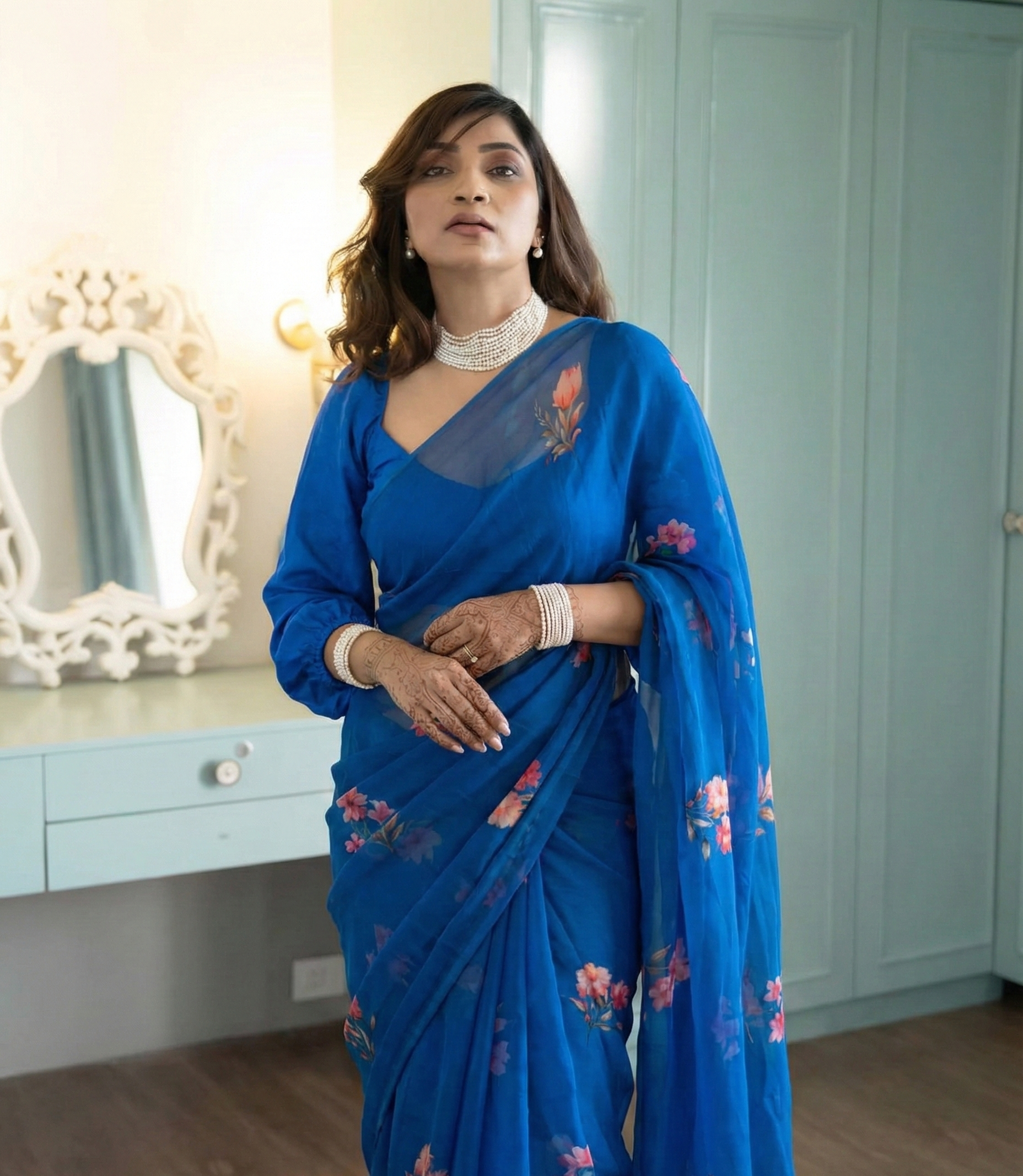 Woman wearing a blue saree with floral patterns in a room with light blue walls.