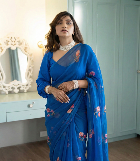 Woman wearing a blue saree with floral patterns in a room with light blue walls.