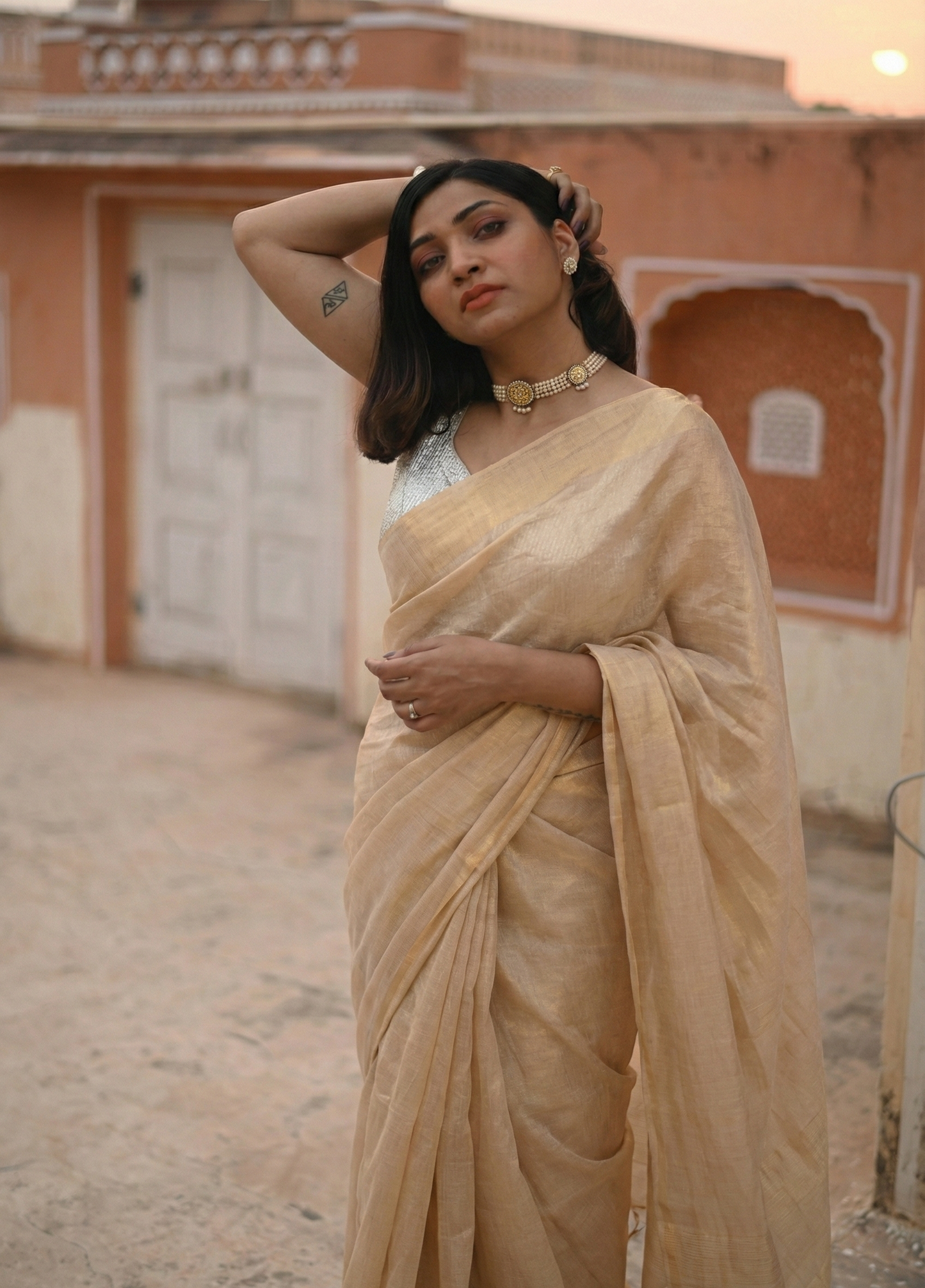 Woman in a beige saree standing in front of an architectural building.