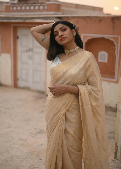 Woman in a beige saree standing in front of an architectural building.