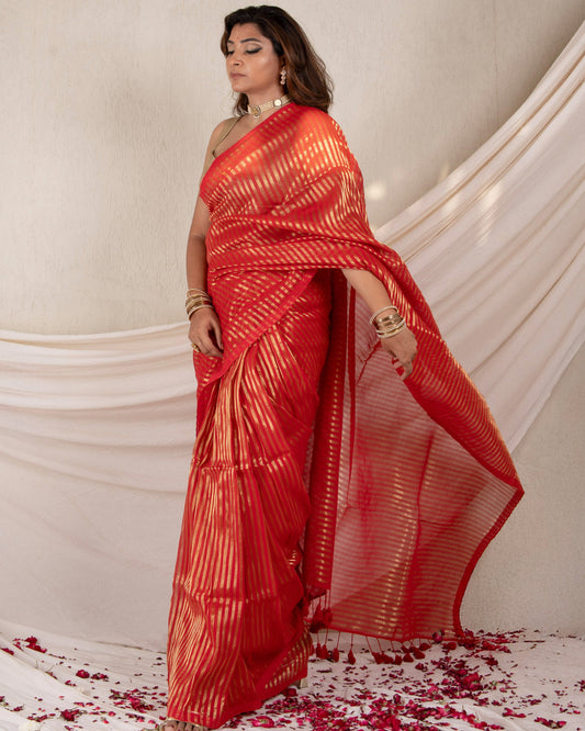 Woman in a red saree with white patterns standing against a white draped backdrop.