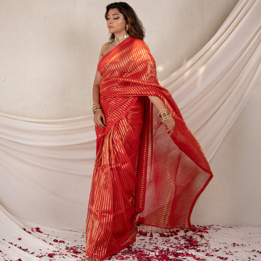 Woman in a red saree with white patterns standing against a white draped backdrop.