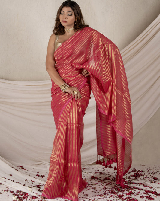 Woman in a red saree standing against a beige draped fabric background