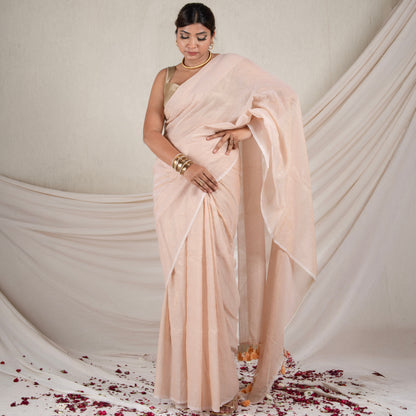 Woman in a beige saree standing against a white draped backdrop with rose petals on the floor.
