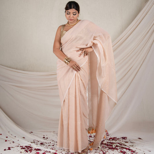 Woman in a beige saree standing against a white draped backdrop with rose petals on the floor.