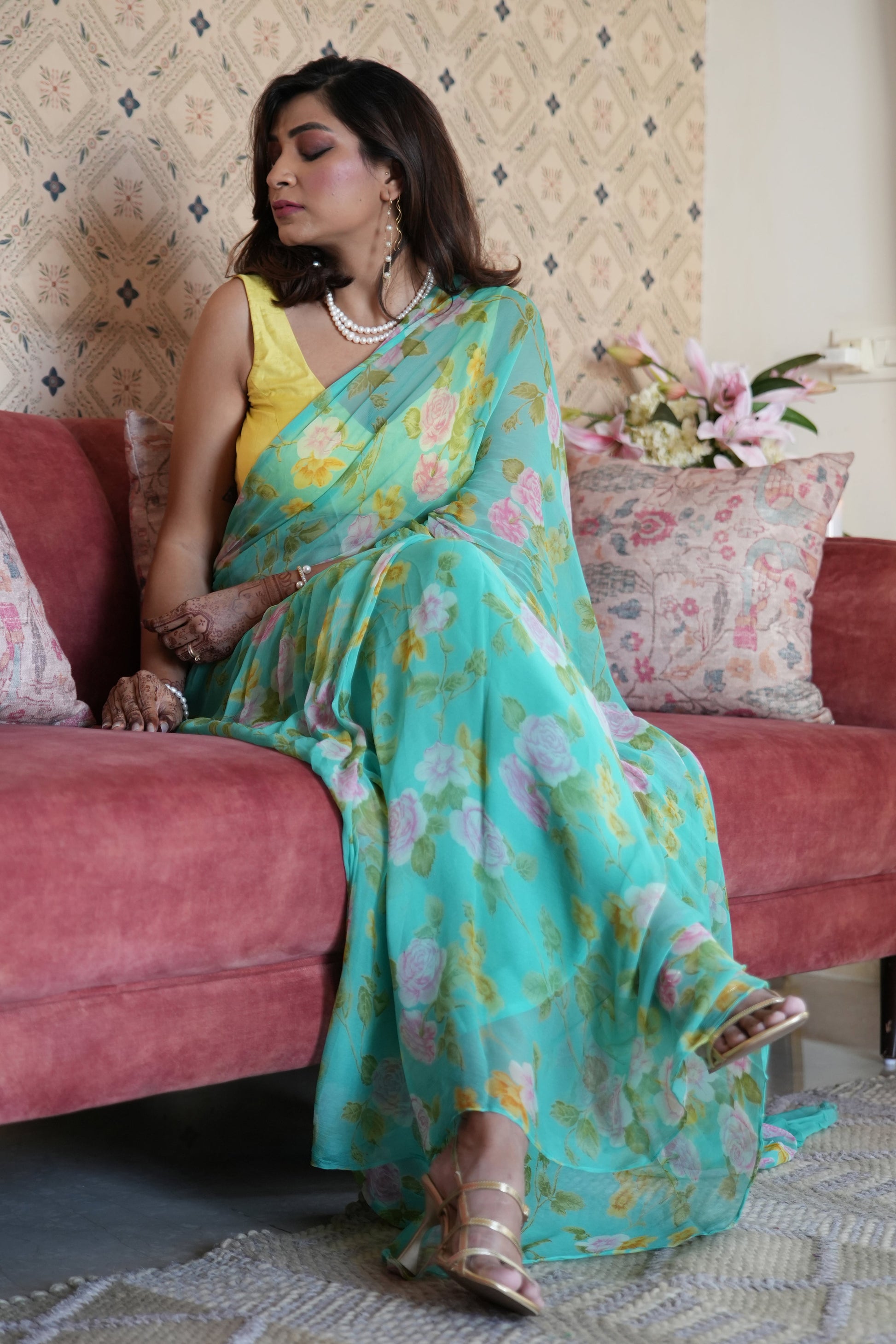 Woman in a floral saree sitting on a pink couch in a living room.