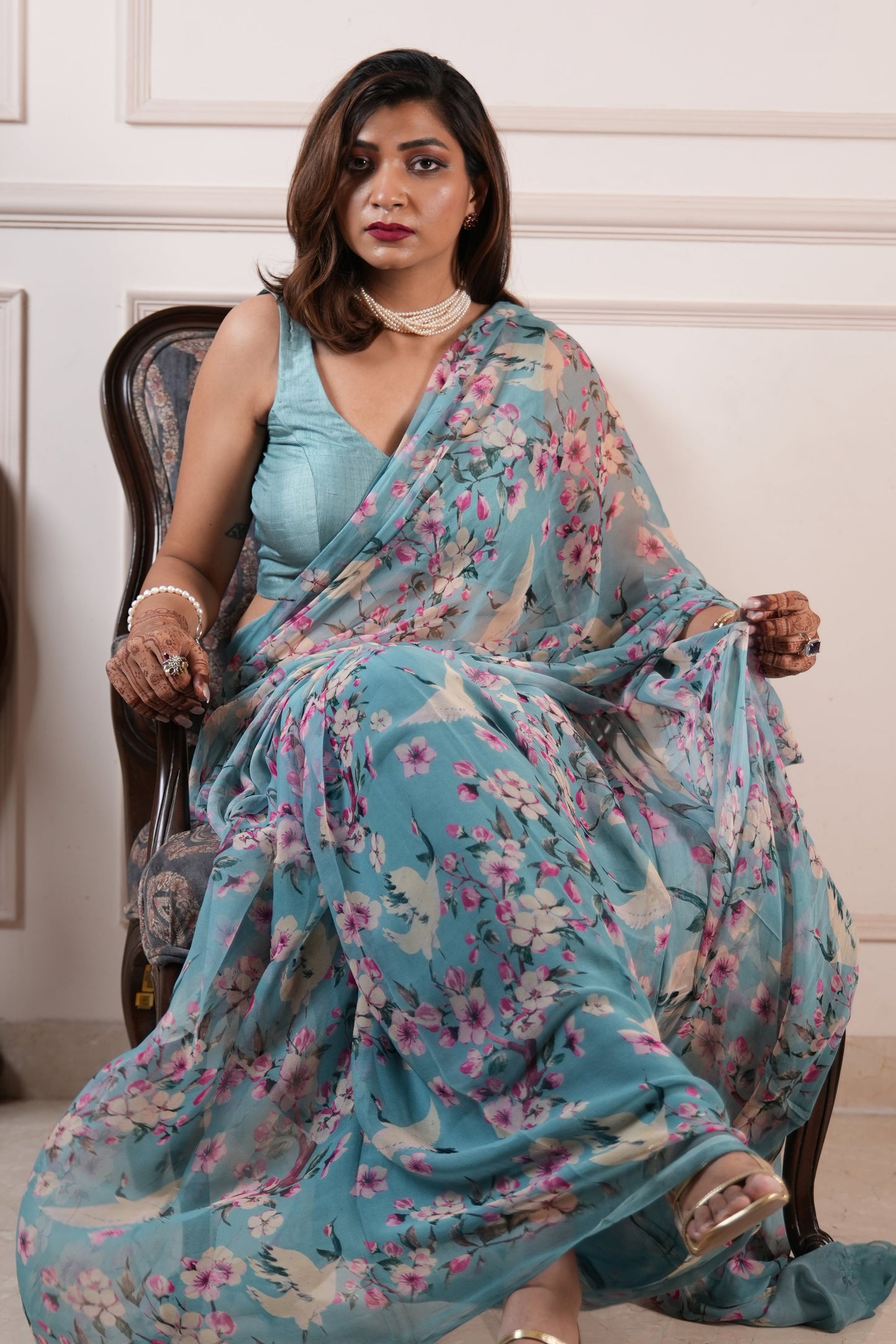 Woman wearing a blue floral saree sitting on a chair.