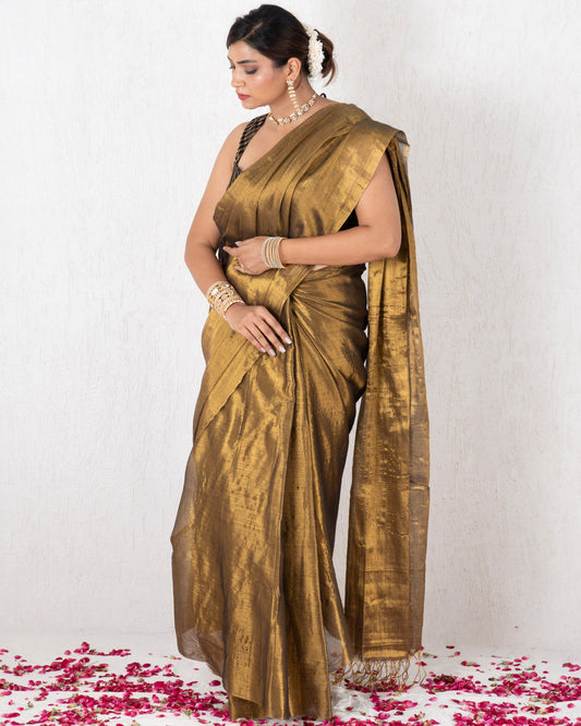 Woman in a gold saree standing on a white background with pink petals at her feet