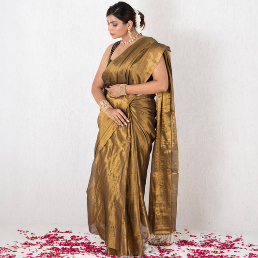 Woman in a gold saree standing on a white background with pink petals at her feet
