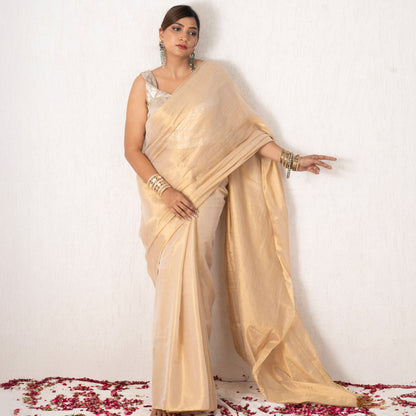 Woman in a beige saree standing on a white background with red flower petals at the base.