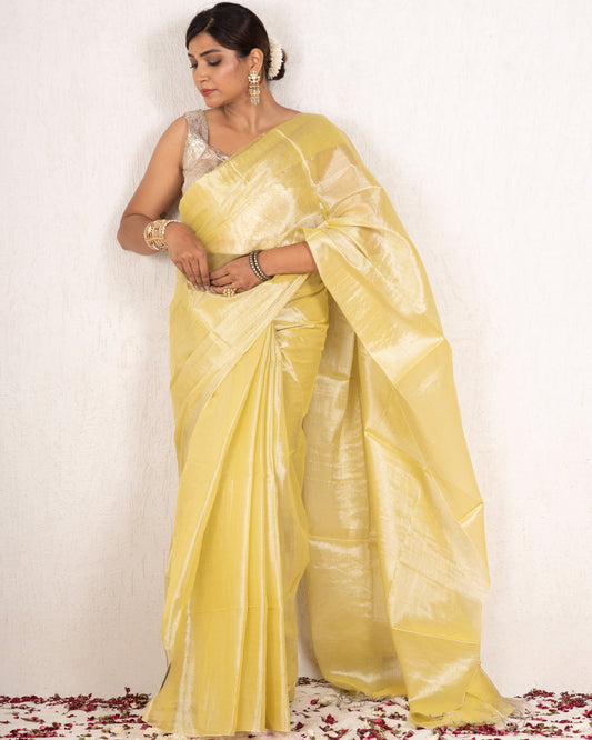 Woman in a yellow saree standing on a white background with rose petals at the base.