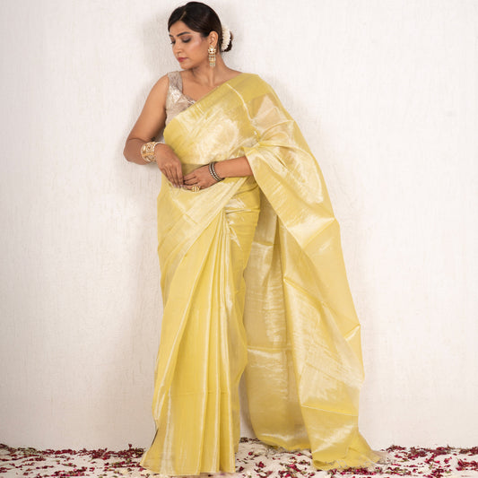Woman in a yellow saree standing on a white background with rose petals at the base.