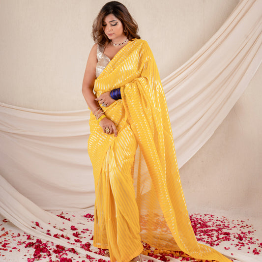 Woman in a yellow saree standing on a floor with red flower petals, draped against a white curtain.