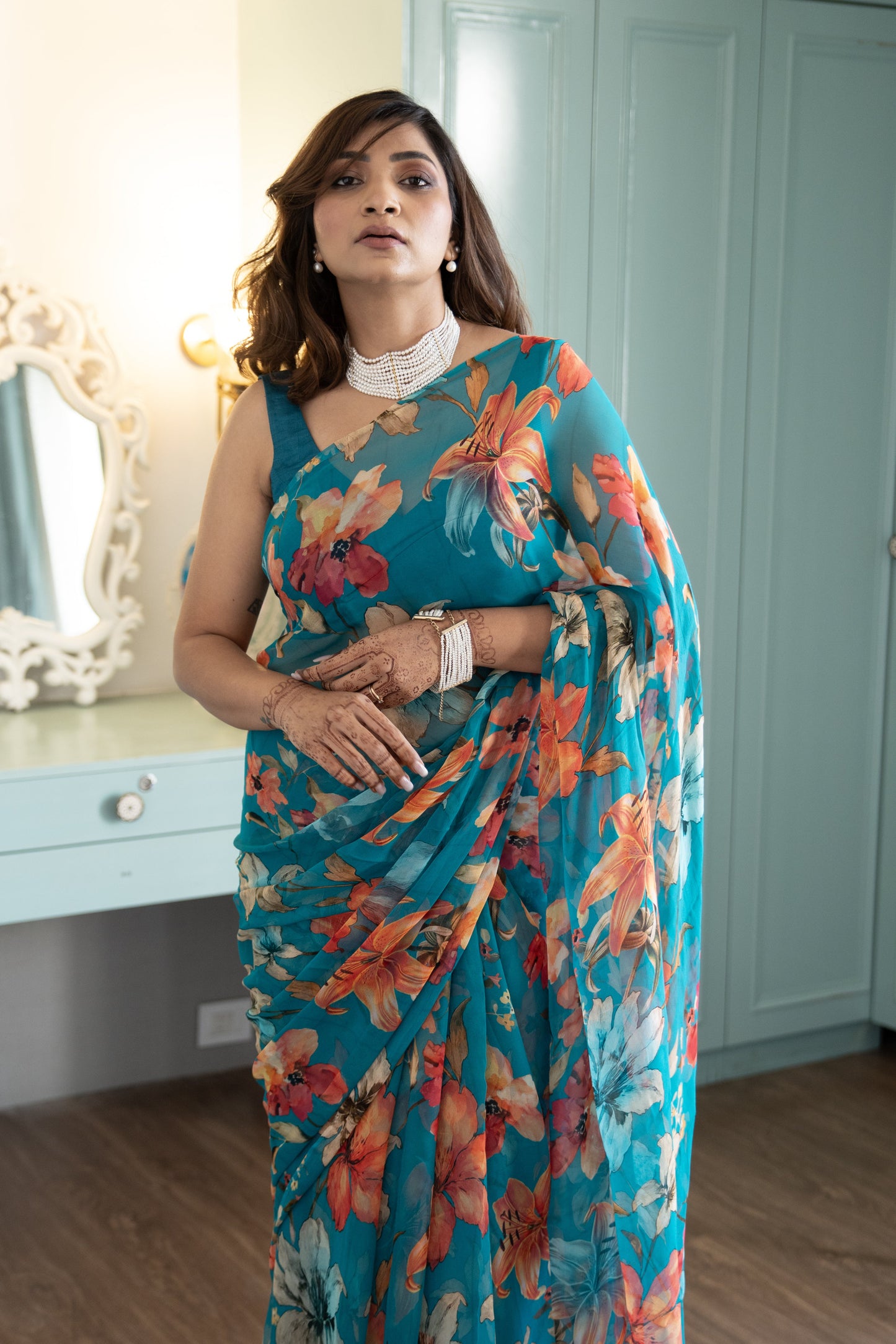 Woman wearing a blue floral saree in a room with a mirror and wardrobe.