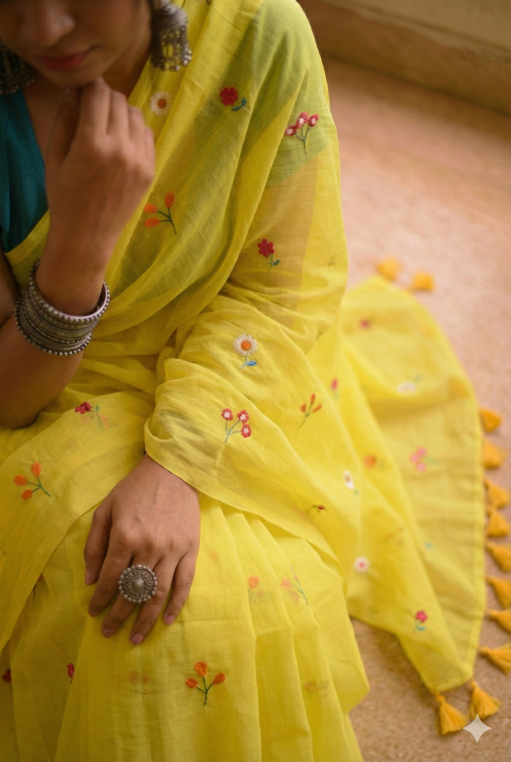 Person wearing a yellow saree with floral embroidery on a wooden floor.