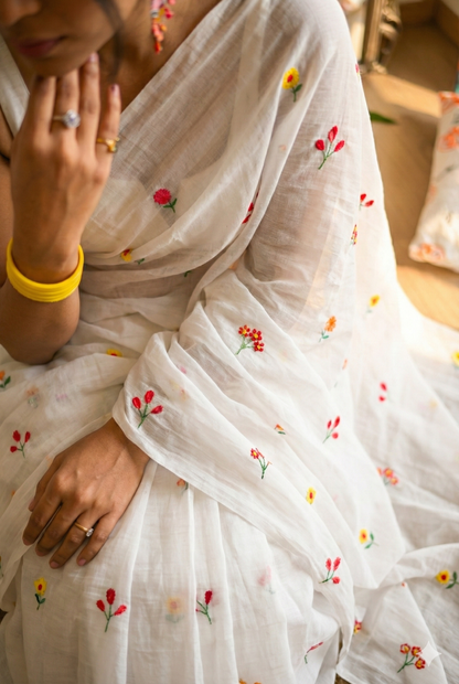 Person wearing a white saree with floral embroidery, close-up of hands.