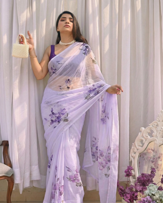 Woman wearing a light purple saree with floral patterns in a decorated room.