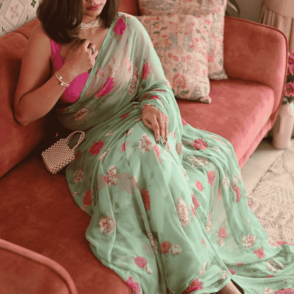 Woman in a floral saree sitting on a pink couch with floral cushions.